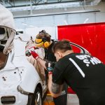 Mechanicy w ubraniach ochronnych pracują nad renowacją karoserii białego samochodu